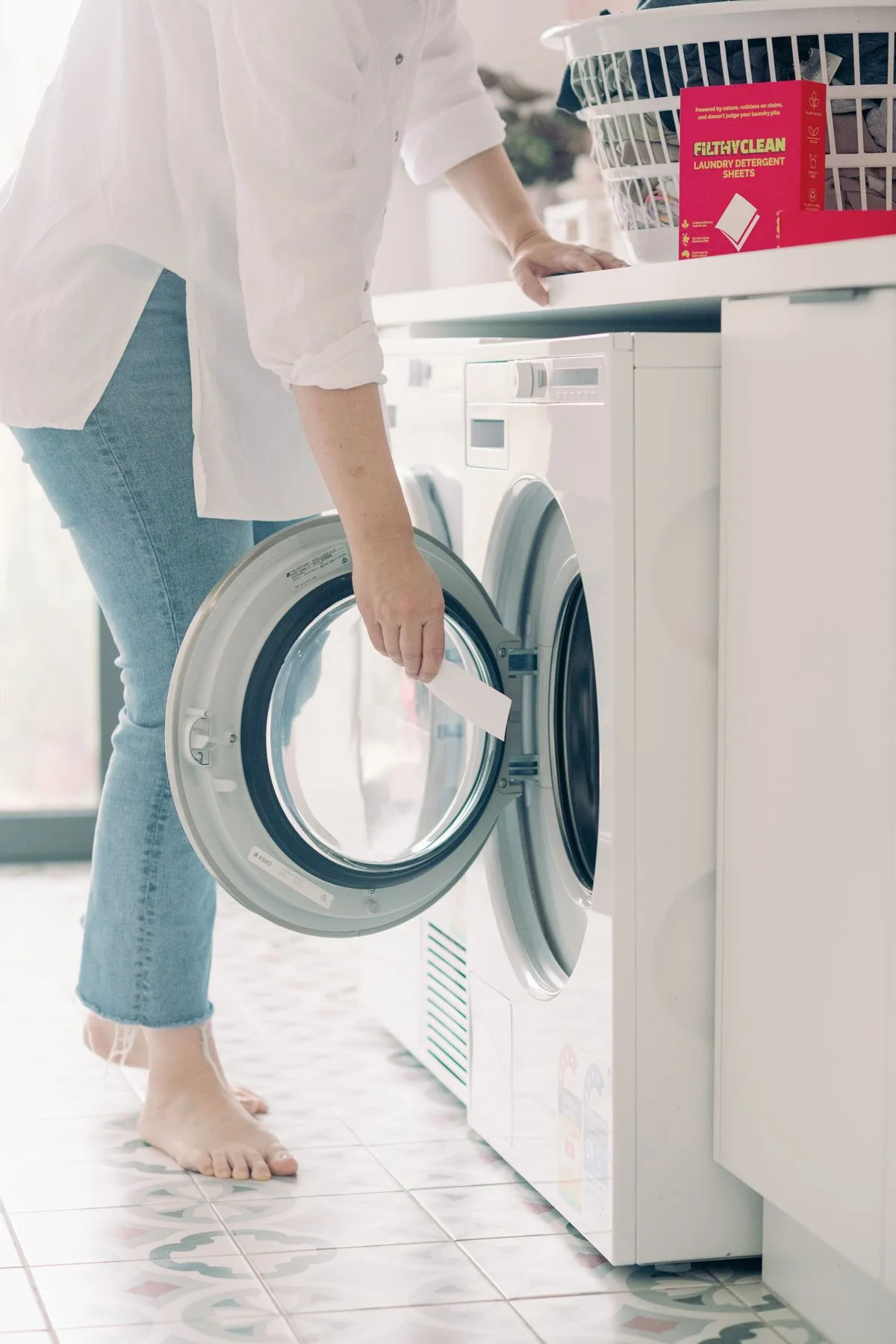 Woman placing one Filthy Clean laundry detergent sheet into a front-loading washing machine drum.